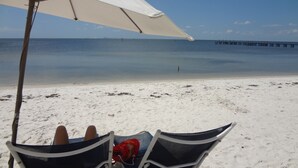 A beach scene with a white umbrella, a chair, and a person reclining. - Beautiful New Luxury Townhome with Private Beach and Swimming Pools  (Ruskin)