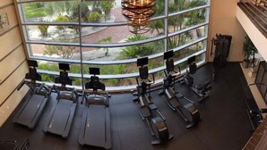 A gym with treadmills and exercise equipment, large windows with a view of greenery and a courtyard. - Beautiful New Luxury Townhome with Private Beach and Swimming Pools  (Ruskin)