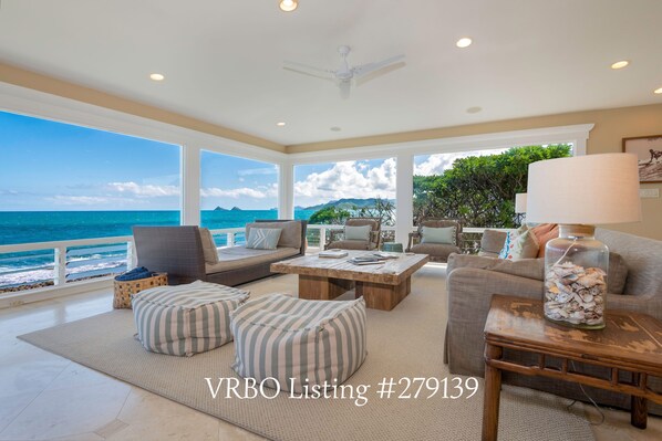 A spacious living room with a large window overlooking the ocean, furnished with a sofa, armchairs, and a coffee table.