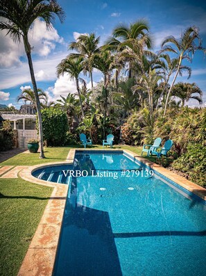 A swimming pool with a clear blue water surface, surrounded by palm trees and green grass.
