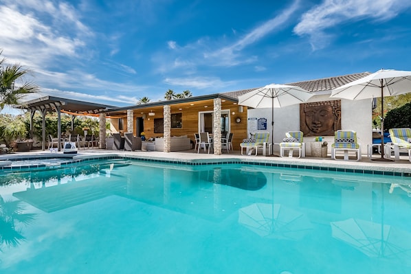 A pool area with lounge chairs and umbrellas, a Buddha statue, and a covered seating area with a view of the pool. - PS Murphy: Updated, Modern and Comfortable Desert Home (Palm Springs)