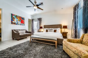 A bedroom with a bed, a bench, a sofa, a ceiling fan, and a painting on the wall. - PS Murphy: Updated, Modern and Comfortable Desert Home (Palm Springs)