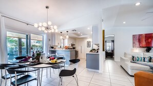 Cozinha moderna com armários brancos, área de jantar com cadeiras pretas e sala de estar com sofá branco.