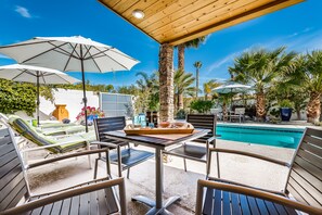 An outdoor pool area with lounge chairs, umbrellas, and a table with a tray of snacks. - PS Murphy: Updated, Modern and Comfortable Desert Home (Palm Springs)