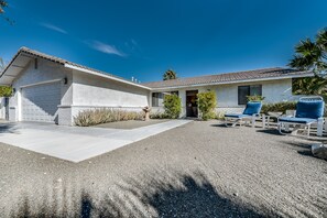 A single-story house with a garage, a covered patio area with two blue chairs, and a gravel driveway. - PS Murphy: Updated, Modern and Comfortable Desert Home (Palm Springs)