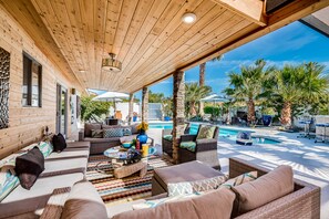 A covered outdoor seating area with wicker furniture, a pool, and palm trees. - PS Murphy: Updated, Modern and Comfortable Desert Home (Palm Springs)