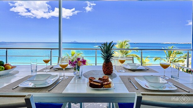 A table set for breakfast with a view of the ocean, a pineapple, and tropical flowers. - Le Papillon on the beach (Simpson Bay)