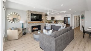 A modern living room with a fireplace, a large grey sofa, and a kitchen in the background.