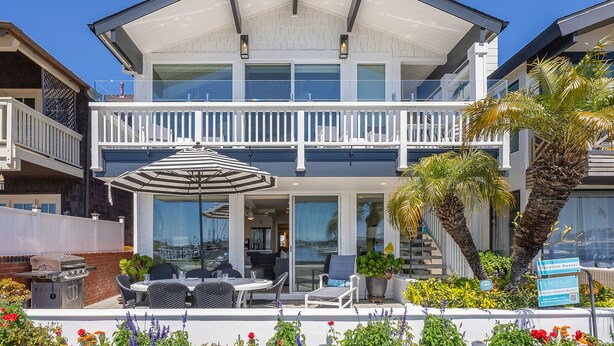 A two-story building with a balcony, outdoor seating, and a sign indicating vacation rental availability.
