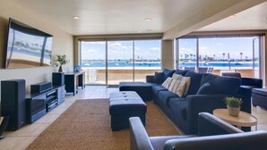 Una sala de estar moderna con un televisor grande, asientos cómodos y vistas a la playa.