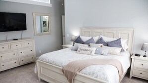 A bedroom with a large bed, a dresser, a nightstand, a TV, and a mirror. - Beautiful Remodeled Home by Ski Resorts & Shopping (Sandy)