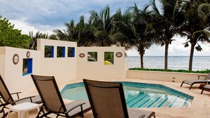 A poolside area with lounge chairs, a small table, and a view of the ocean.
