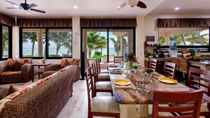 A dining area with a view of the ocean, wicker furniture, and a kitchen area with a water dispenser.
