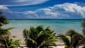 A beach with clear turquoise water, palm trees, and a partly cloudy sky.