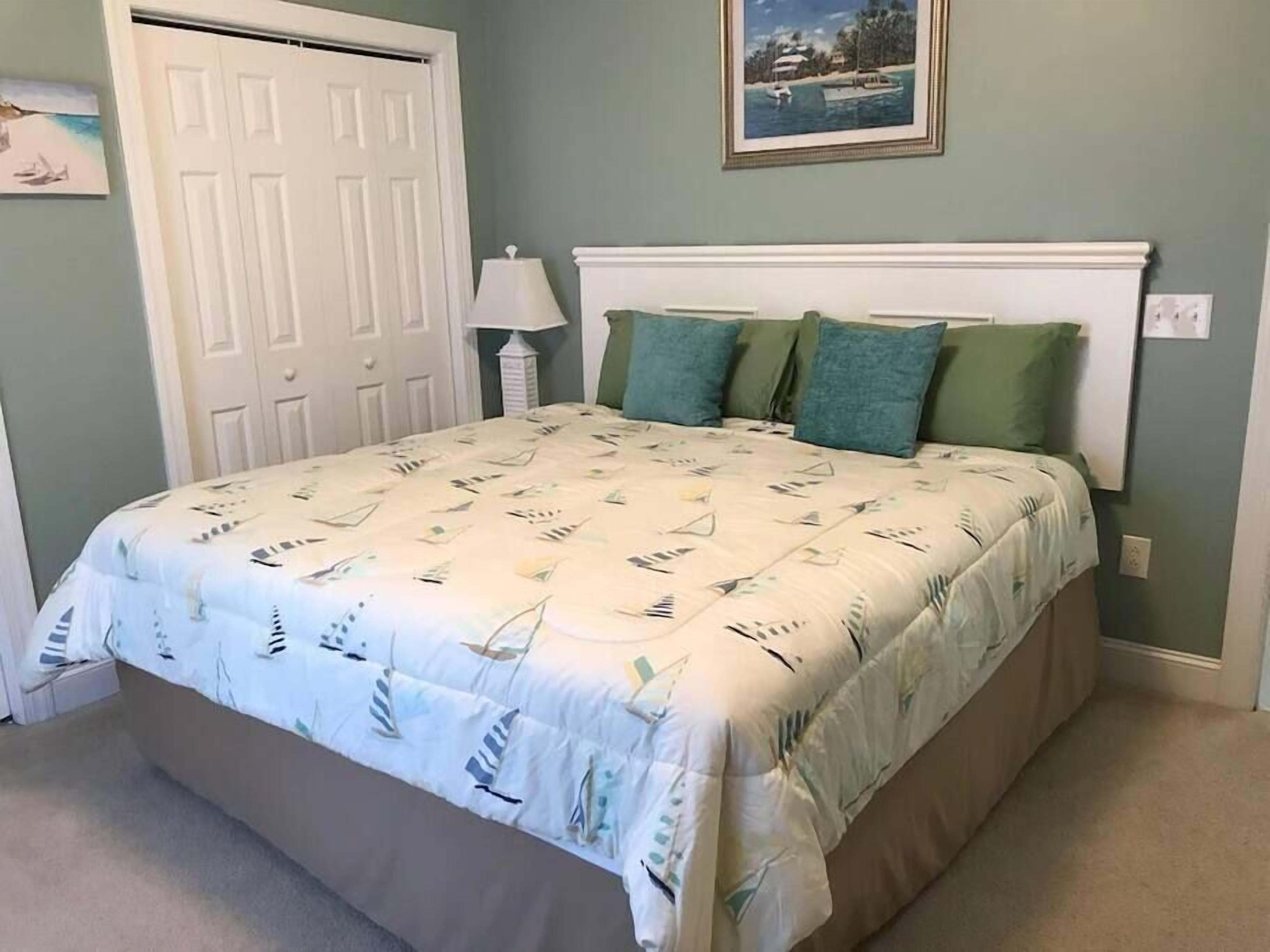 Quarto com cama, porta, luminária e quadro na parede.