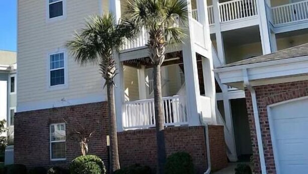 A two-story building with a white exterior, a balcony on the second floor, and a garage.