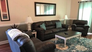 A living room with a black leather sofa, a matching armchair, and a coffee table. There is a mirror on the wall and a lamp on a side table.