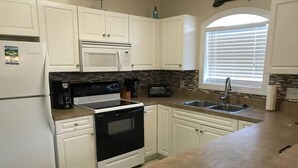 A kitchen with white cabinets, a microwave, a stove, a coffee maker, and a window with blinds.