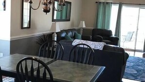A dining area with a table and chairs, a chandelier, a sofa, and a ceiling fan.