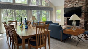 A spacious living room with a dining area, large windows, a brick fireplace, and a flat-screen TV. - Private, Immaculate 4BR/4BA Home—community pool/tennis, minutes to beach/golf (Hilton Head Island)