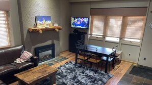 A cozy living room with a fireplace, a television, a dining table with chairs, a sofa, and a rug. - Best Location Ski In/Out Condo @ Boyne Mountain- Walk To Village (Boyne Falls)