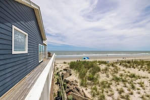 Una casa de playa con terraza de madera, vista al océano y vegetación costera.