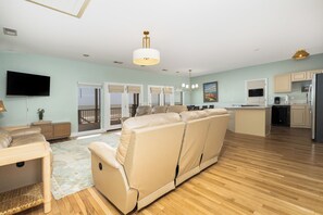 A spacious living area with a sofa, a dining table, a flat-screen TV, and a kitchen with a refrigerator.