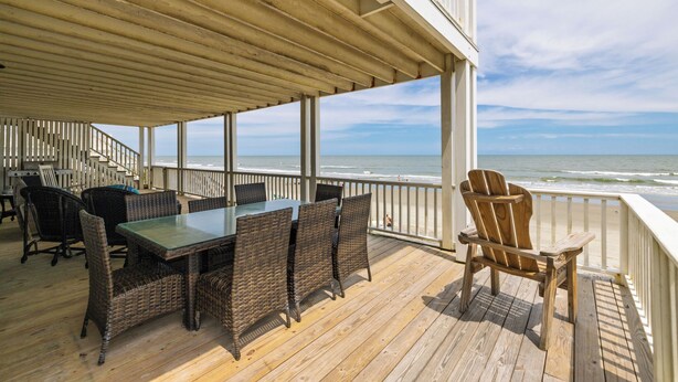 A covered outdoor deck with a table and chairs, overlooking the ocean. - Charleston Coast Vacations "Seascape Wonder" (Folly Beach)