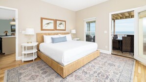 A bedroom with a large bed, a small bedside table, a nightstand, a patterned rug, and a view of the balcony. - Charleston Coast Vacations "Seascape Wonder" (Folly Beach)