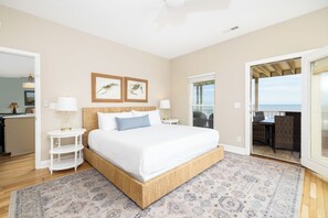 A bedroom with a large bed, a small bedside table, a nightstand, a patterned rug, and a view of the balcony.