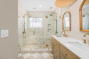 Un baño con ducha de vidrio, tocador con lavamanos y un espejo grande.