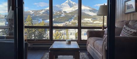 A cozy living room with a large window offering a view of a snow-capped mountain and a ski resort.
