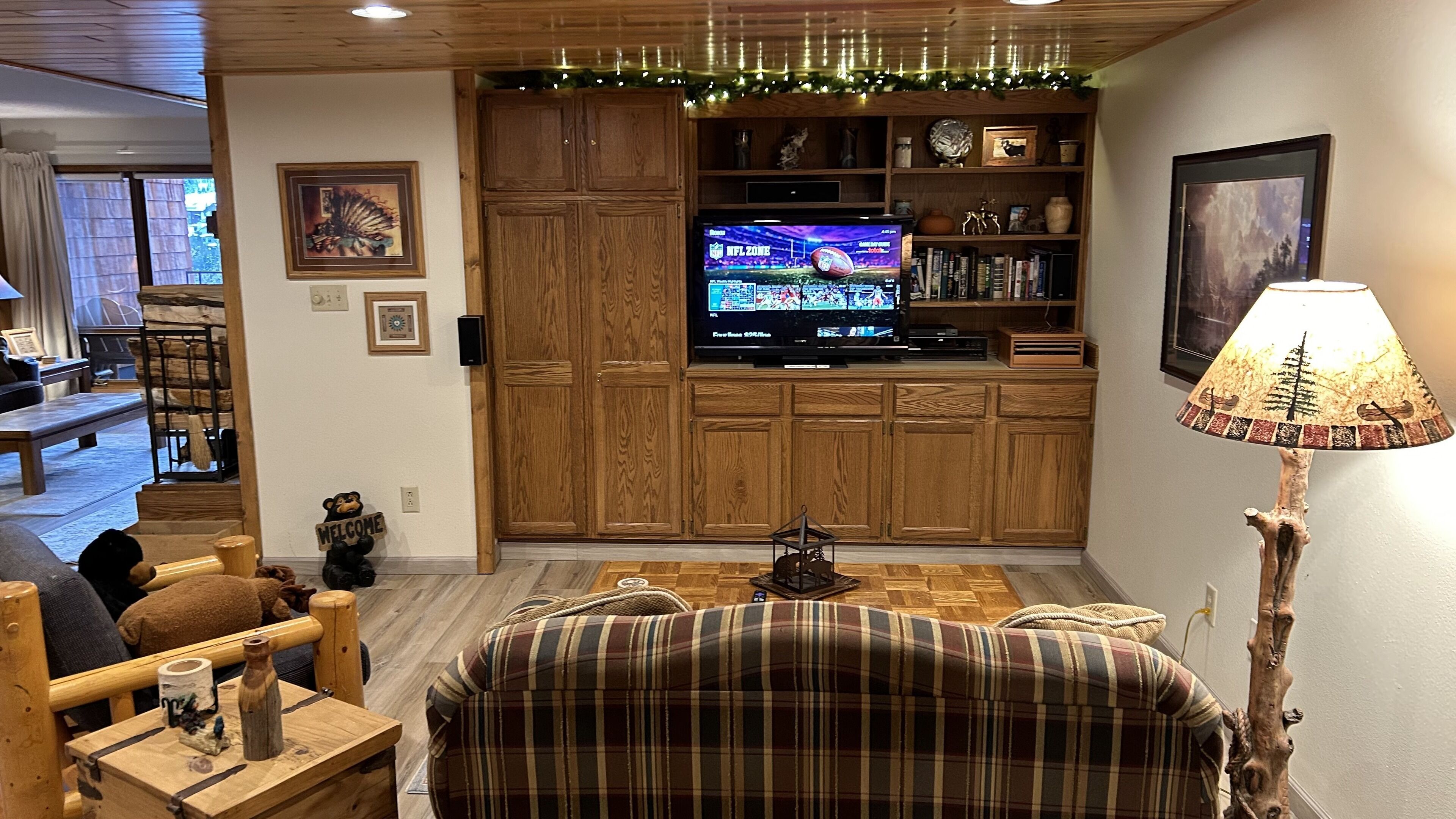 A cozy living room with a plaid sofa, wooden entertainment center, and a television displaying a sports event.