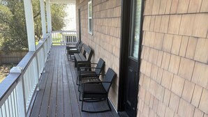 Une véranda couverte avec un plancher en bois, une balustrade blanche et une porte dotée d’une fenêtre.