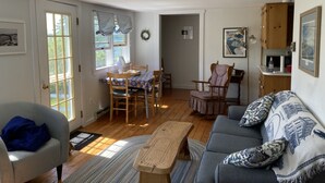 A cozy living room with a sofa, a dining table with chairs, and a wooden cabinet. - Oceanfront Cottage in Milbridge ~ME~ (Milbridge)