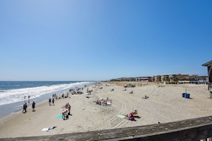 A beach with people sunbathing and swimming, a lifeguard tower, and buildings in the background.