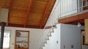 Interior de madeira com escada e parede branca com relógio.