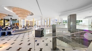 A modern lobby with a glass staircase, seating areas, and a reception desk.