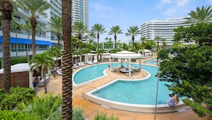 A swimming pool surrounded by palm trees and lounge chairs, with high-rise buildings in the background.