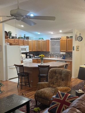 A modern kitchen with wooden cabinets, a central island, and a dining area with a patterned sofa and a table.