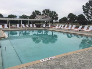 Una piscina con una marca de profundidad de 99 centímetros, rodeada de sillas de descanso blancas y una zona cubierta con techo.