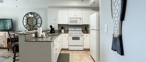 A modern kitchen with white cabinets, a central island, a microwave, and a refrigerator.
