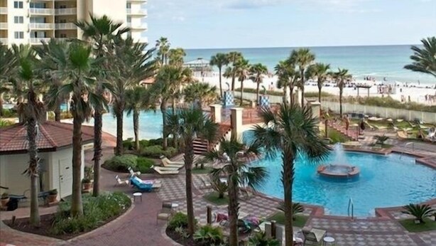 A resort with a large pool, palm trees, and a view of the beach.
