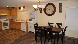 Une cuisine avec des meubles de rangement en bois, une table à manger avec des chaises, une horloge et un lustre.