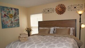 Une chambre avec un grand lit, un tableau au mur et une lampe sur pied.