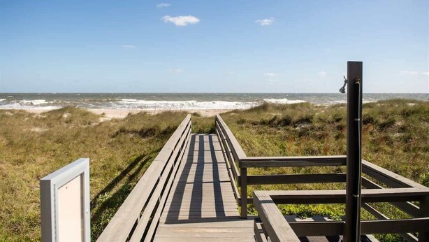 A wooden boardwalk leading to a beach with dunes and a clear sky.