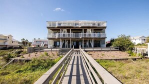A multi-story building with balconies, a central staircase, and a wooden walkway leading to the entrance.