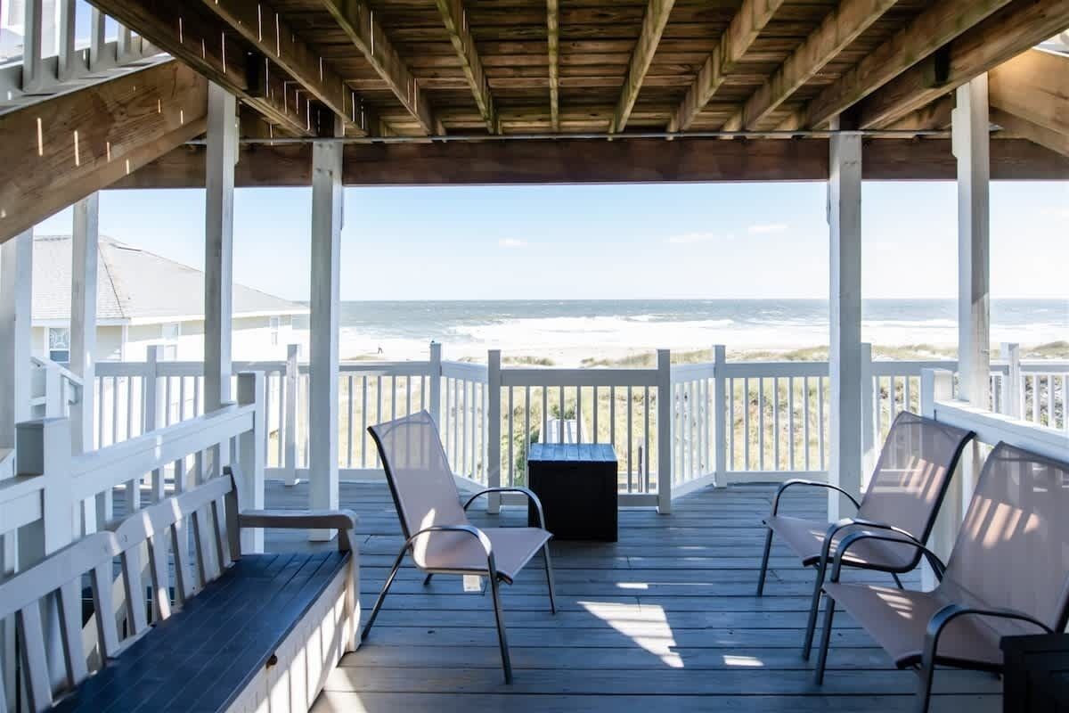 Eine Holzterrasse mit weißen Geländern mit Blick auf einen Strand.