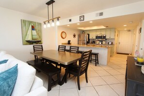 A modern kitchen with a central island, a dining area with a wooden table and chairs, and a living room with a white sofa. - Shore to Please - Condo 402: A cozy oceanfront  2-bedroom retreat in South Padre Island. (South Padre Island)