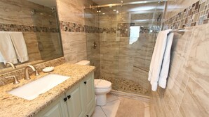 Une salle de bain moderne avec une douche à parois de verre, un comptoir en granit, des toilettes et un grand miroir.